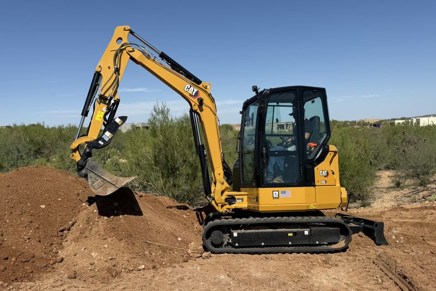 A Caterpillar 304 mini excavator digging into red Arizona soil, with the spoil piled alongside the cut.