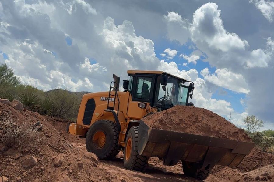 A wheel loader carrying a full bucket of excavated soil across a job site under heavy cloud.